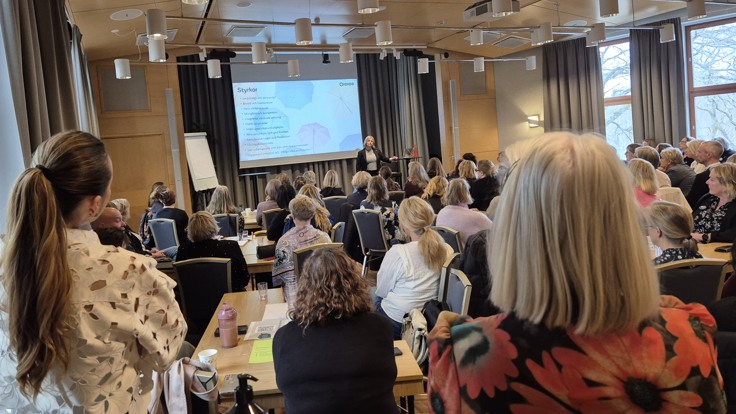 Många personer i ett rum, vända mot en stor skärm.