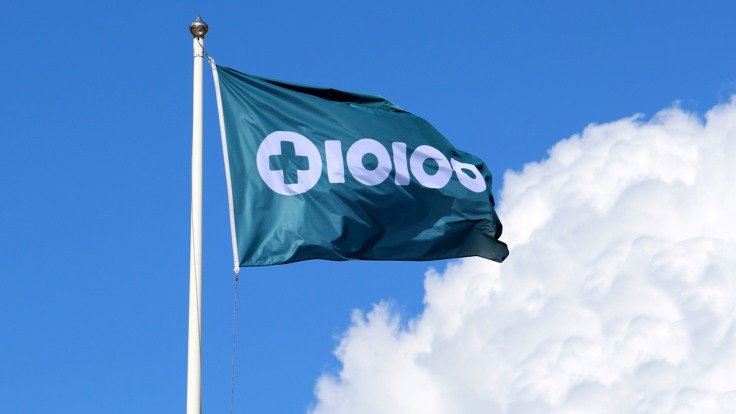 Flagga med Tiohundras logotyp. Blå himmel med sommarmoln.