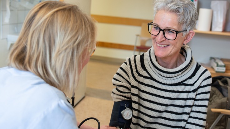 Läkare tar blodtryck på patient som ser glad ut. 