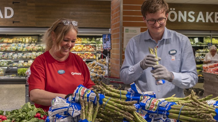 Två personer i arbetskläder lägger upp sparris på grönsaksavdelning